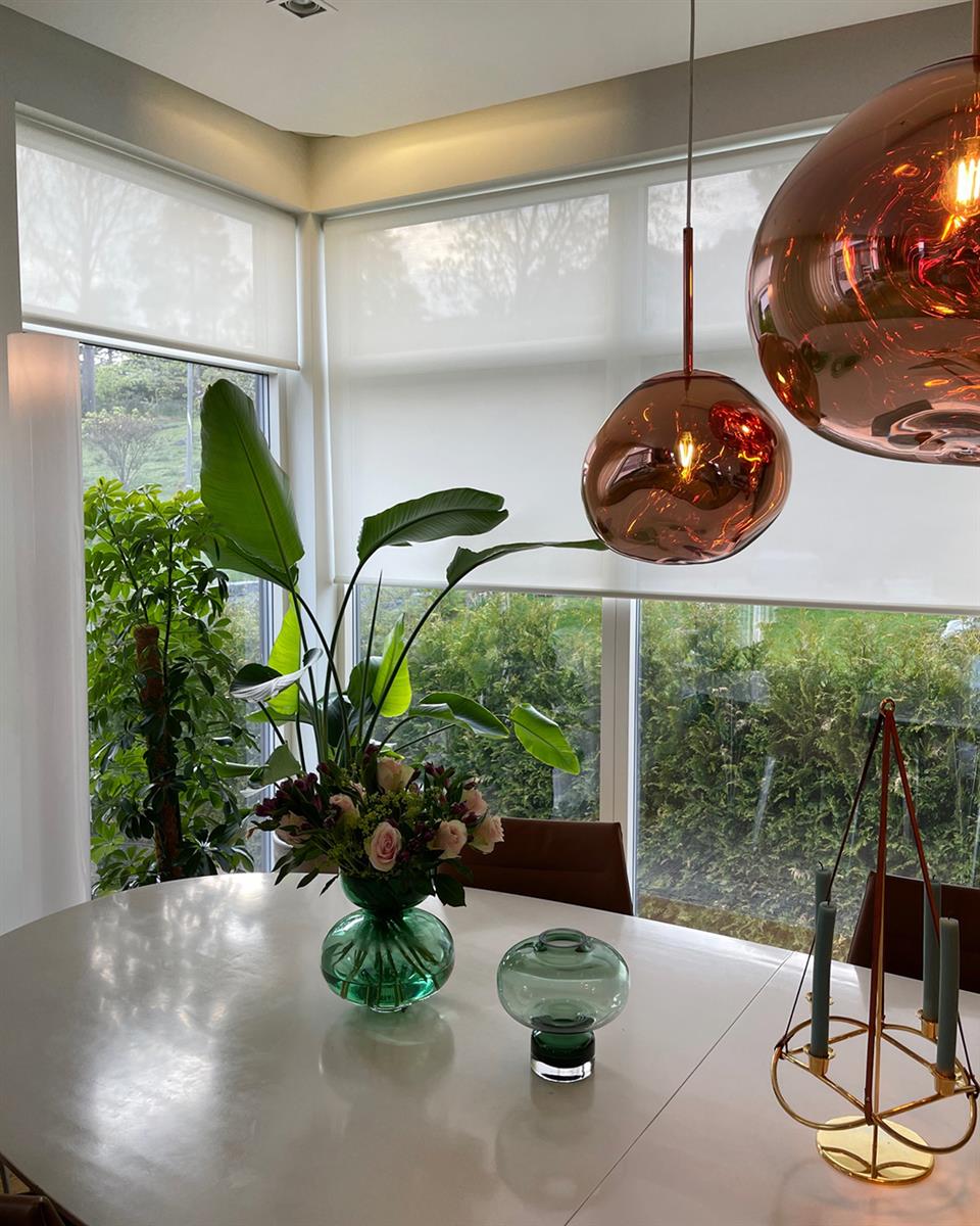 Lyst rom med lysfiltrerende smart rullegardin og hvitt spisebord. Foto.